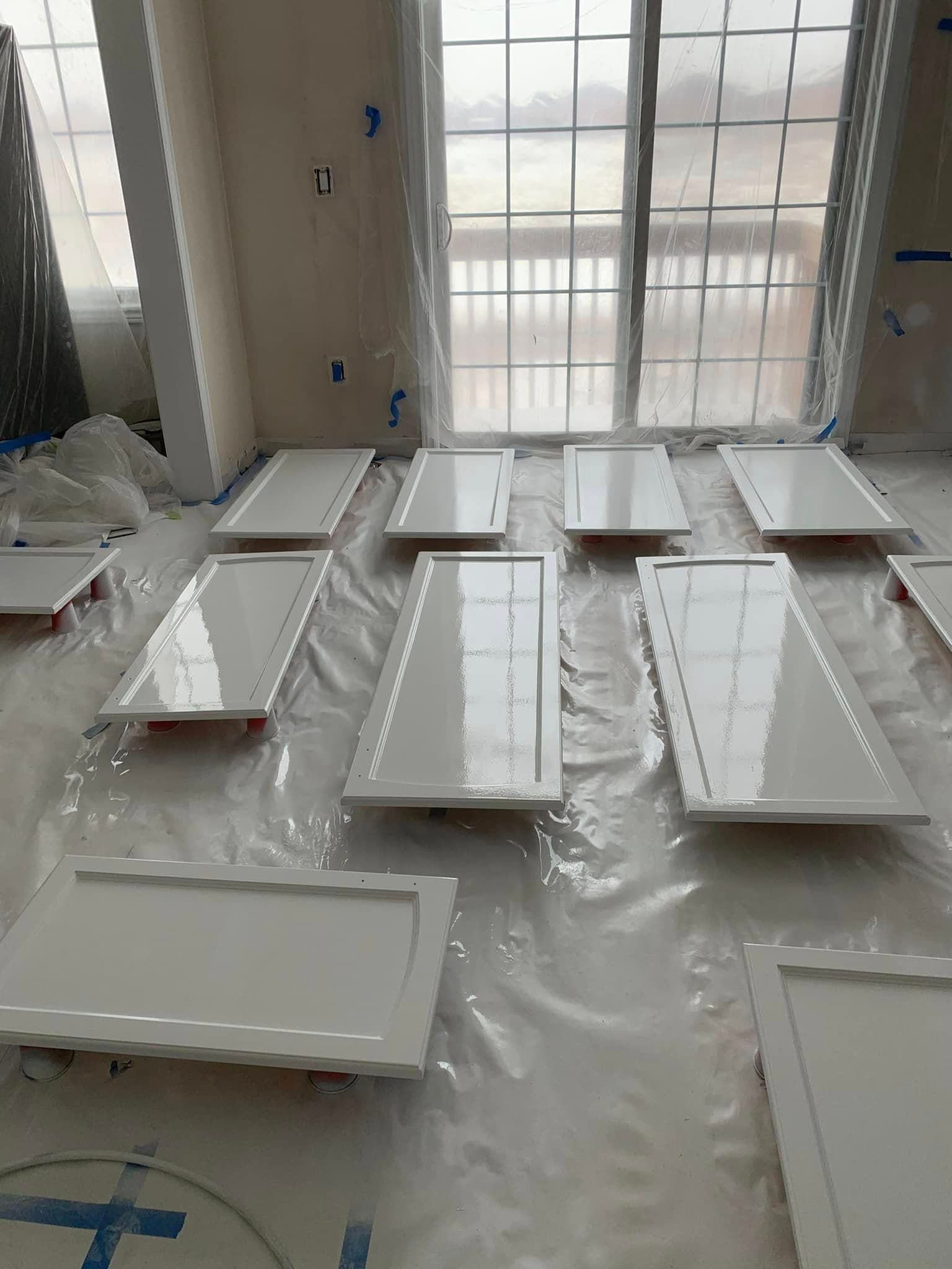Freshly painted glossy white cabinet doors drying on plastic sheeting in a room under renovation.