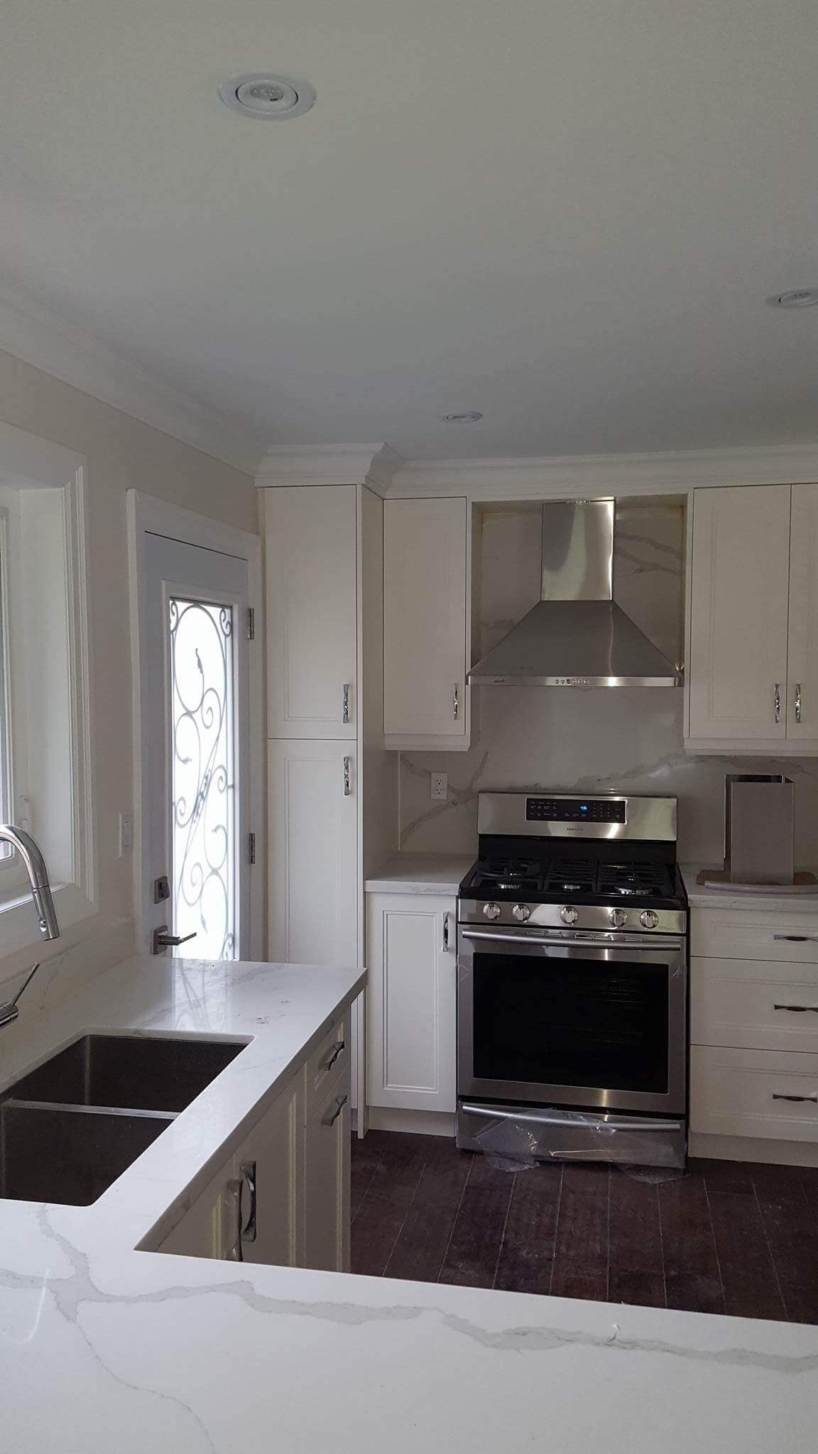 Modern white kitchen featuring stainless steel appliances, marble-patterned countertops, and dark wood floors.