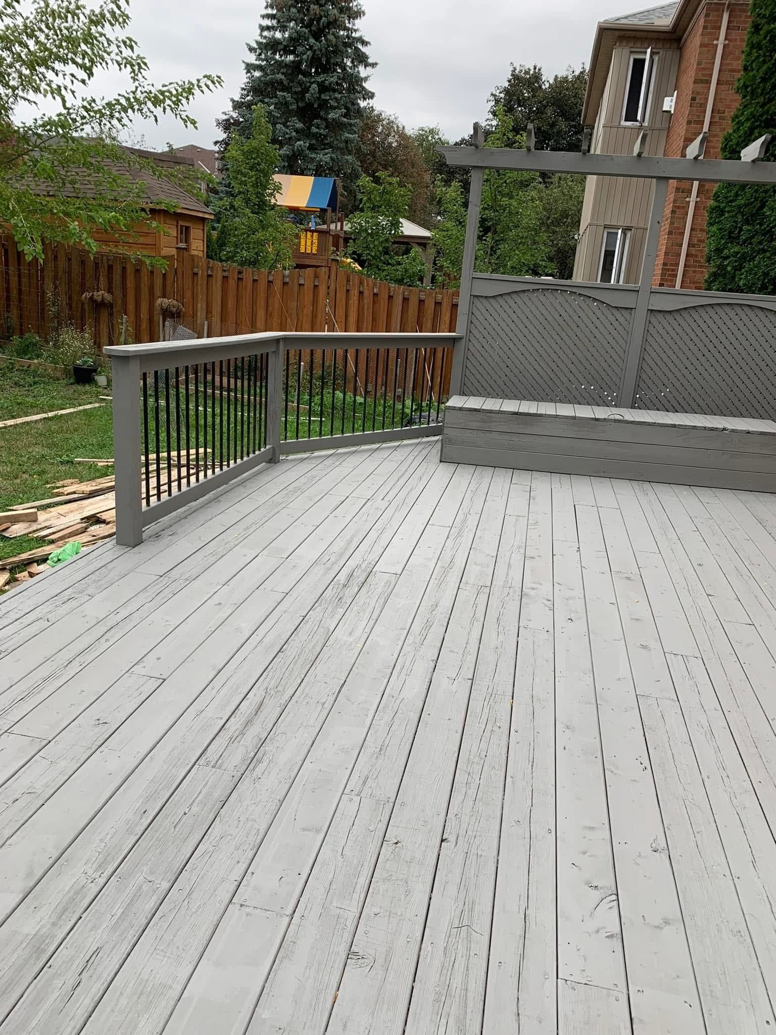Grey-painted wooden deck featuring a built-in bench, lattice privacy screen, and black spindle railings.