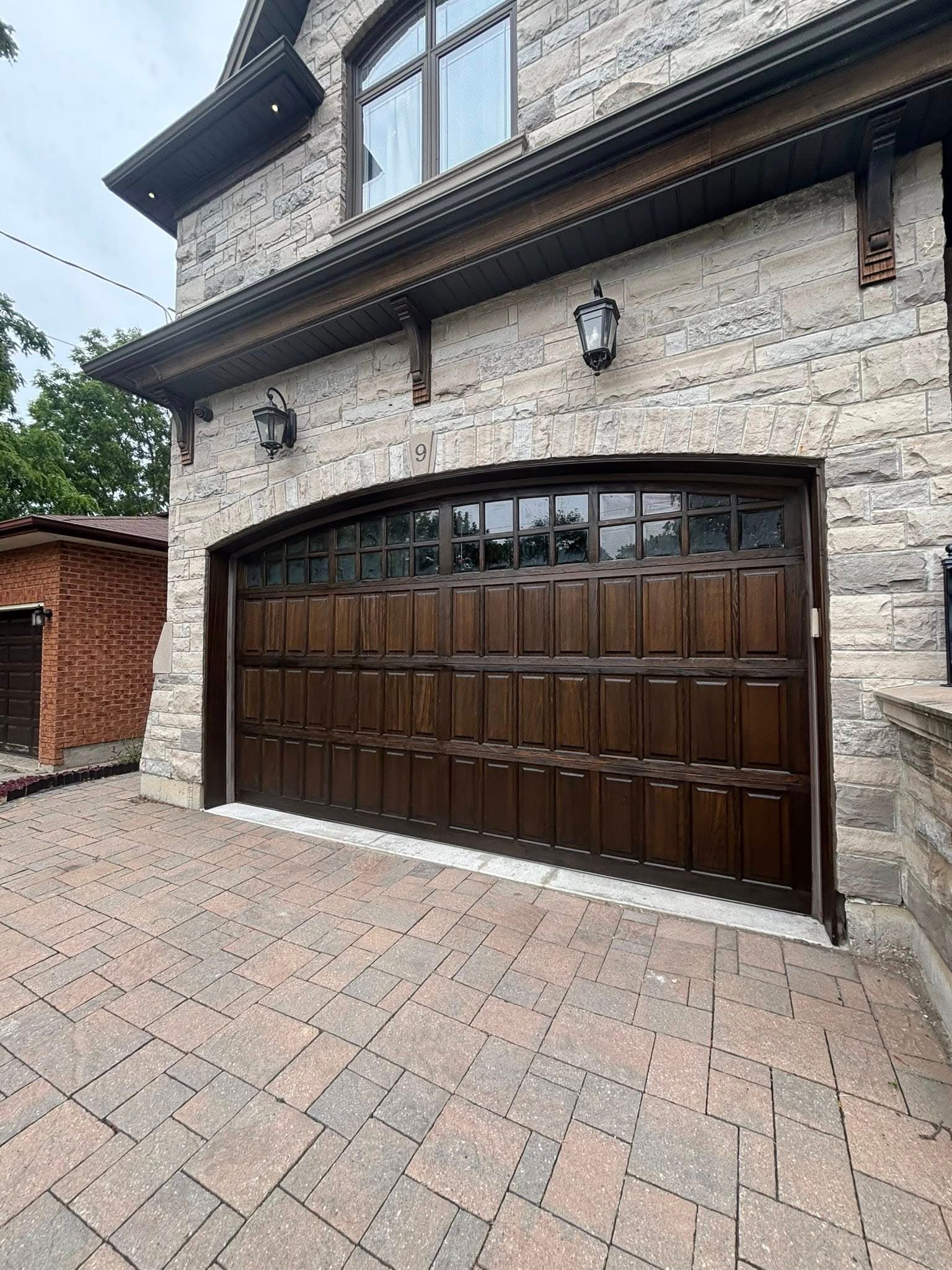 Arched dark wood garage door with small windows on a light stone house exterior.